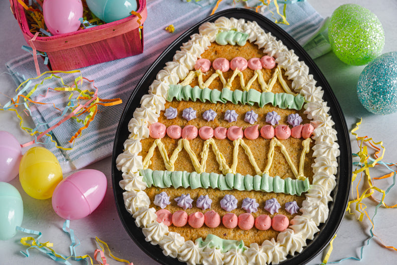 Easter Celebration with Frosted Keto Birthday Cake Cookie Egg Surrounded by Plastic Eggs, Confetti, and Basket